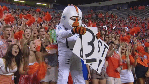 College football fan dressed like astronaut, pretending to blast off, jumps and lands in hedge.